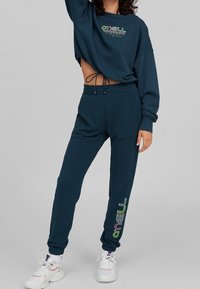 Felpa cropped blu scuro con coulisse, caratterizzata da un logo multicolore. Pantaloni jogger abbinati con stampa del logo sulla gamba.