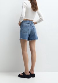 Vaaleansiniset farkkushortsit, joiden reuna on rispaantunut, korkea vyötärö ja takataskut, yhdistettynä mustiin platform-sandaaleihin.