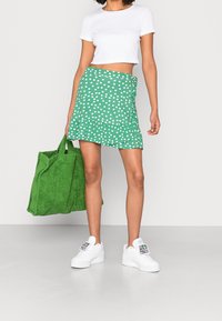 Grønne polkaprikker wrap-nederdel med flæsekant, parret med en simpel hvid crop top. Afsluttet med en struktureret grøn taske og hvide sneakers.