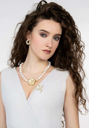 Pearl necklace with a gold floral pendant, accompanied by gold leaf earrings and a decorative brooch. Outfit features a textured white fabric.