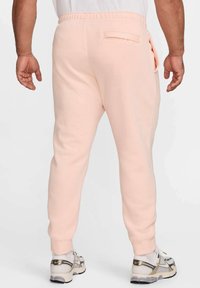 Pantalones de chándal rosa de corte ajustado, con cinturilla elástica y un detalle de bolsillo trasero. Textura suave con puños acanalados.