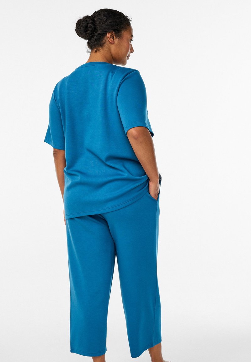 Blaues, kurzärmeliges Oberteil und verkürzte Hose aus weichem, glattem Stoff. Das Outfit hat eine entspannte Passform mit Seitentaschen und einem abgerundeten Saum.