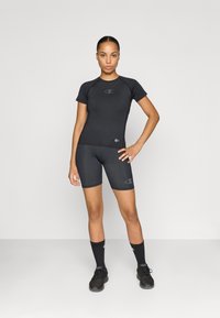 Svart atletisk tröja och shorts i sträckbart material, med logodetaljer på båda plaggen. Modellen har på sig matchande svarta skor och strumpor.