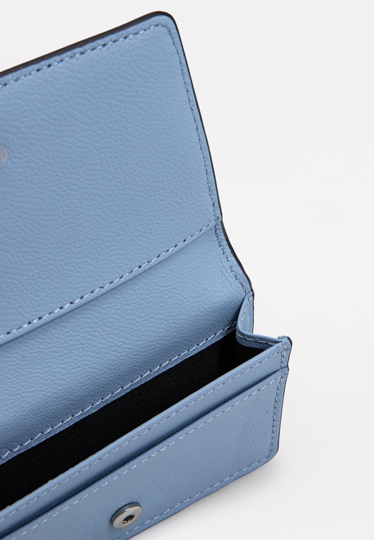 Blaues Lederportemonnaie mit strukturierter Oberfläche, ausgestattet mit einem Druckknopfverschluss und mehreren Kartenfächern, innen mit schwarzem Stoff ausgekleidet.