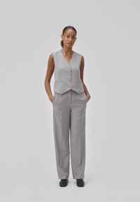 Vesta gri cu decolteu adânc în V și cinci butoane, asociată cu pantaloni largi asortați. Țesătură netedă, design minimalist, fără tipare.