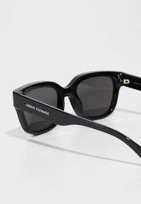 Occhiali da sole neri con una montatura rettangolare spessa, lenti scure e il logo "Armani Exchange" sulle aste laterali. Materiale in plastica liscia.