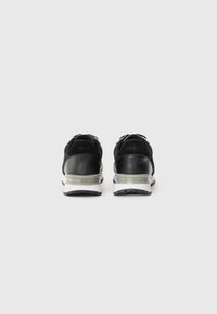 Black sneakers with a combination of suede and leather. Features a white and gray sole, branding on the heel, and a textured finish.