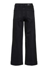 Schwarze Jeans mit weitem Bein, von hinten gezeigt, mit zwei aufgesetzten Gesäßtaschen und einem Leder-Logo-Patch am Bund.