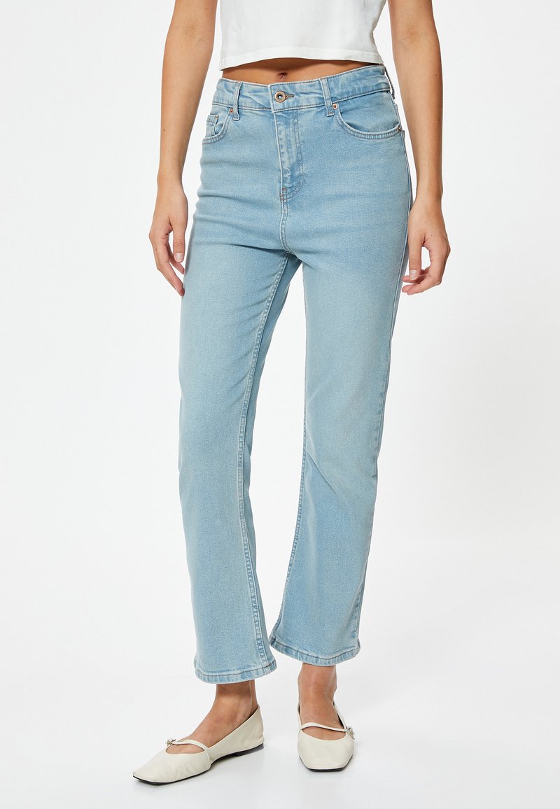 Jeans de tiro alto color azul claro, hechos de mezclilla, con corte recto, que cuentan con bolsillos frontales y cierre de botón. Combinados con zapatos planos blancos.