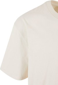 T-shirt en coton beige à manches courtes et col rond. Texture lisse avec un design épuré et simple, sans motifs ni accents visibles.