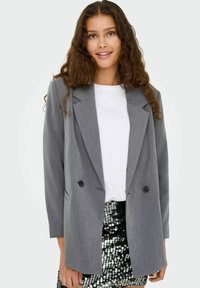 Pelēks dubultā jaka ar izteiktiem uzgaļiem, melniem pogām un garām piedurknēm, apvienota ar vienkāršu baltu T-kreklu un melnu svārku ar pērlītēm.