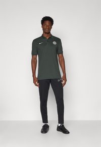 Polo skjorte i mørkegrøn med krave og logo, parret med sorte træningsbukser og sorte sneakers, med en slim fit design.