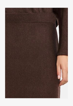 Dunkelbrauner gestrickter Pullover mit geripptem Bündchen und Saum sowie einem subtilen Schimmer. Das Material wirkt weich und strukturiert. Eine Hand ist sichtbar.