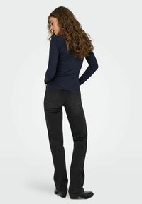 Navy gestreifter Langarm-Top, kombiniert mit schwarzen geraden Jeans. Die Jeans besitzen Gesäßtaschen und leicht ausgestellt geschnittene Säume. Glatte, strukturierte Stoffqualität.