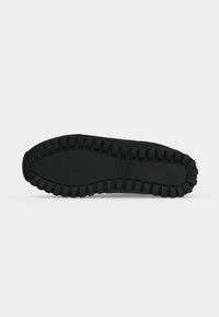 Semelle de chaussure noire avec un motif de rainures profondes et le logo « BOSS » embossé près du centre, à plat sur fond blanc.