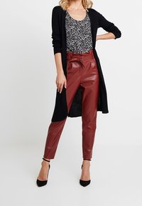 Černý dlouhý kardigan, vršek s leopardím potiskem a vysoké červenohnědé kalhoty z umělé kůže s páskem na zavazování. Černé lodičky na jehlovém podpatku dokončují outfit.