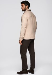 Giacca in misto lana beige con colletto e bottoni, abbinata a pantaloni marrone scuro e stivaletti neri in suede, vista da dietro.
