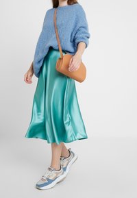 Ljusblå stickad tröja, teal satinkjol, tan axelremsväska och flerfärgade kraftiga sneakers. Mjuka texturer med flödande tyg.