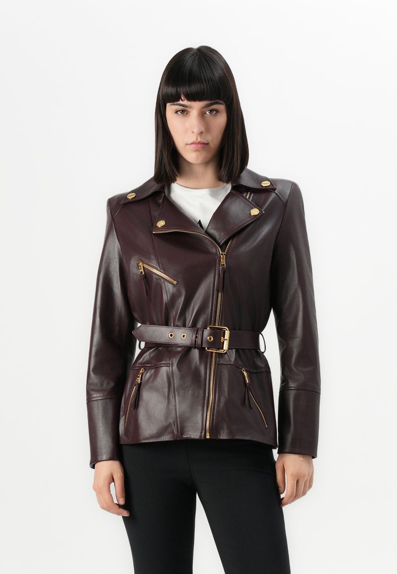 Burgundy leather jacket with a fitted design, gold zip closures, and a belted waist. Features four zip pockets and broad lapels.