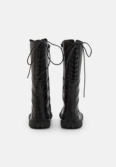Bottes noires à lacets, hauteur genoux, avec une finition laquée brillante, présentant des coutures diagonales, un bout arrondi et une semelle en caoutchouc texturée.