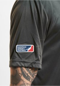 Tamsiai pilkos spalvos sportinė marškinė su trumpomis rankovėmis, ant rankovės esantis stačiakampis "Europos futbolo lyga" emblema raudonos, mėlynos ir baltos spalvų.