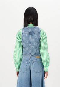 Denim overall with a faded blue finish, featuring floral detailing on the back, paired with a green and white striped blouse.