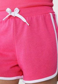 Shorts en coton rose avec cordon blanc, présentant une texture lisse et un contraste blanc le long des bords.