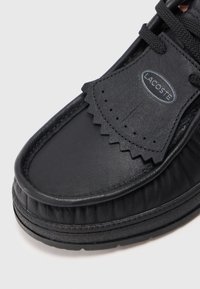 Mustmust nahkane Lacoste loafer, millel on tekstuuriga servad, dekoratiivsed perforatsioonid ja paks gommi tallal, valgel taustal.