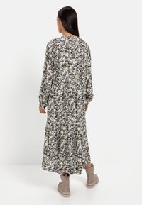 Langes Blumenkleid in Weiß, Grün und Grautönen, mit geraffter Taille, Ballonärmeln und fließendem Saum. Braune Knöchelstiefel runden den Look ab.