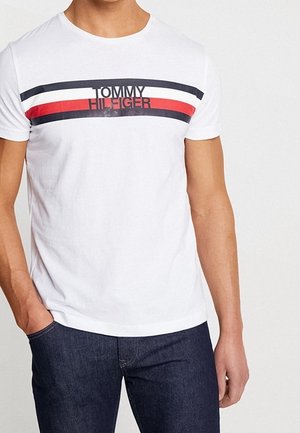 White short-sleeve t-shirt features a bold multi-colored stripe pattern with red, blue, and white. Logo print in black across the chest.