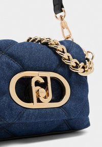 Geantă din denim cu accesorii aurii, textură matlasată, curea din lanț și un accent proeminent cu logo circular pe față.