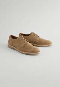 Brown suede lace-up shoes with a smooth finish, rounded toe, and contrasting stitching on a light brown rubber sole.