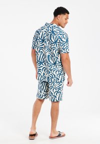 Korte mouw button-up shirt en bijpassende shorts in een blauw-wit abstract bladpatroon, gemaakt van lichte stof met een comfortabele pasvorm.