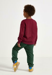 Burgundyröd sweatshirt med långa ärmar, kombinerad med gröna byxor och gula sneakers med blå detaljer. Slätt tyg och avslappnad passform.