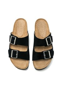 Sandalias de ante negro deslizantes que presentan dos hebillas ajustables, plantilla texturizada en tono marrón y una suela negra resistente. Diseño plano con dedo del pie y talón abiertos.