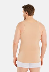 Beige tank top made of smooth fabric, featuring wide shoulder straps and a fitted design, paired with white shorts. Back view shown.