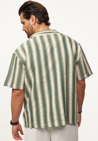 Kurzarmhemd mit gestreiftem Muster in Grün und Creme, mit strukturiertem Gewebe und Kragen. Die Rückansicht zeigt die Designdetails des Hemdes.