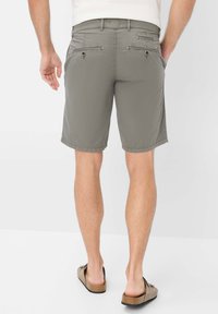 Pantaloni corti grigi con vestibilità rilassata, caratterizzati da due tasche posteriori con patta e cuciture decorative. Indossati con scarpe marroni senza lacci.