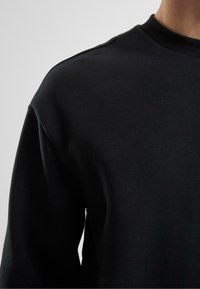 Schwarzer Pullover mit Rundhalsausschnitt, langen Ärmeln, weicher Textur und lockerer Passform, ohne sichtbare Logos oder Muster.