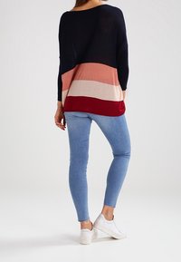 Dzianinowy top z szerokim dekoltem i rękawami do łokcia, ozdobiony poziomymi paskami w kolorach granatowym, różowym, beżowym i bordowym. W połączeniu z niebieskimi dżinsami i białymi trampkami.