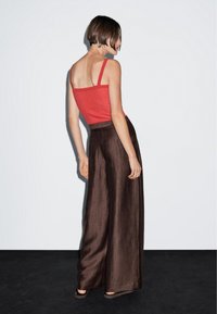 Rode geribbelde tanktop gecombineerd met luchtige, donkerbruine wijde broek. De stof heeft een gestructureerde afwerking en de outfit is eenvoudig en elegant.