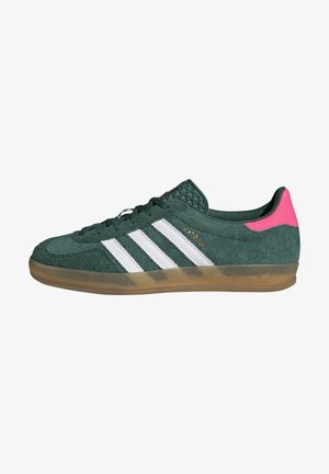 Sneaker Adidas verde scuro con strisce bianche, suola marrone traslucida e linguetta posteriore rosa acceso, vista laterale.