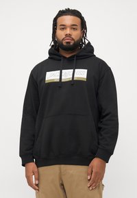 Black hoodie with a front pocket, drawstring hood, and white and gold "JACK & JONES" logo on the chest. Soft, textured fabric.