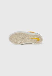 Vit sneaker sula med zigzag mönster för grepp, med en gul Nike swoosh och en tan gummibeläggning vid hälen.