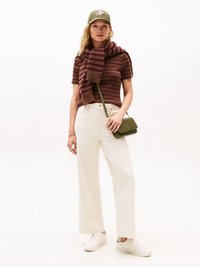 Écharpe en tricot violet et marron à rayures, casquette de baseball verte olive, haut ajusté à manches courtes, large pantalon blanc et tennis blanches. Sac bandoulière.