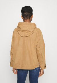 Tan hooded jacket in a soft, textured fabric. Features a relaxed fit, buttoned cuffs, and a simple, streamlined design.