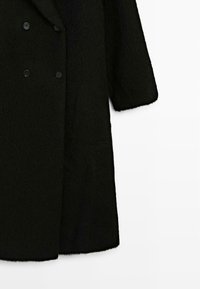Manteau en mélange de laine noir avec un design à double boutonnage, de grandes boutons, et un tissu lisse et texturé avec des manches larges et une coupe droite.