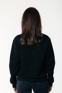 Black sweatshirt with long sleeves and ribbed hem, viewed from the back. Dark jeans and wavy brown hair are visible. Plain white background.