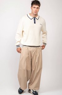 Beige vida byxor, vit ribbad stickad tröja med marinblå krage och muddar. Modellen bär marinblå och vita sneakers med en minimalistisk design.