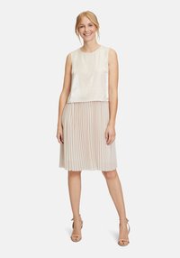 Ärmelloses Kleid mit einem glänzenden, cremigen Oberteil und einem plissierten, hellbeigen Rock. Der Stoff ist weich mit einer strukturierten Oberfläche und hat eine fließende Silhouette.